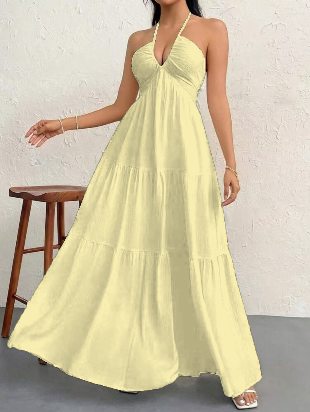 Woman wearing a yellow halter neck dress against a white brick wall.
