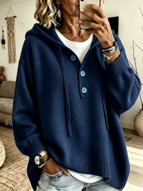 A woman takes a mirror selfie wearing a navy blue knit hooded sweater with a buttoned placket over a white t-shirt and light-wash jeans.