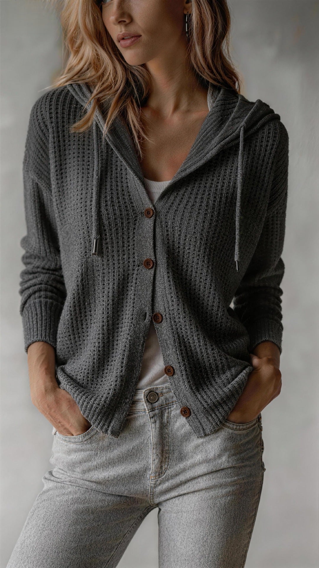 Woman wearing a gray knitted cardigan with brown buttons against a neutral background