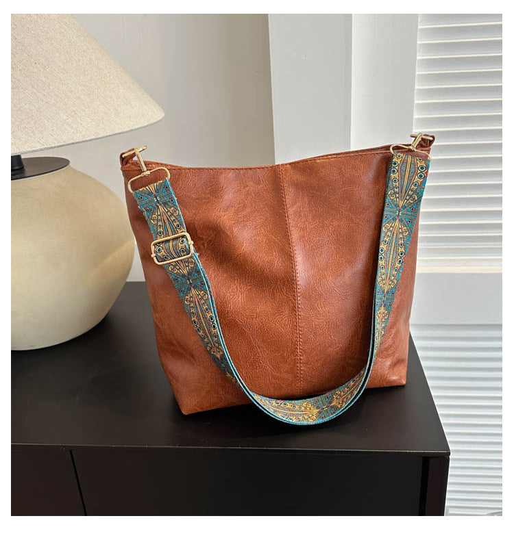 Brown leather handbag with decorative strap on a dark surface