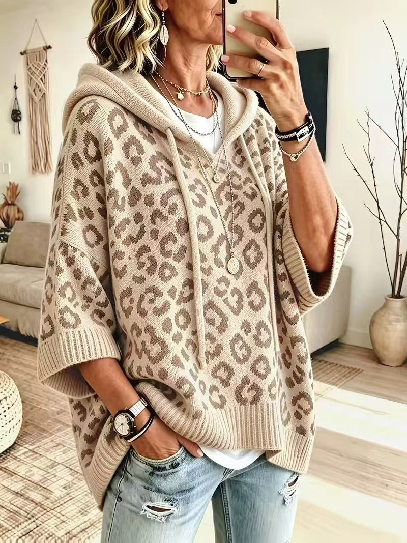 A woman takes a mirror selfie wearing a beige and brown leopard-print knit hoodie sweater with wide three-quarter sleeves, paired with light-wash distressed jeans.