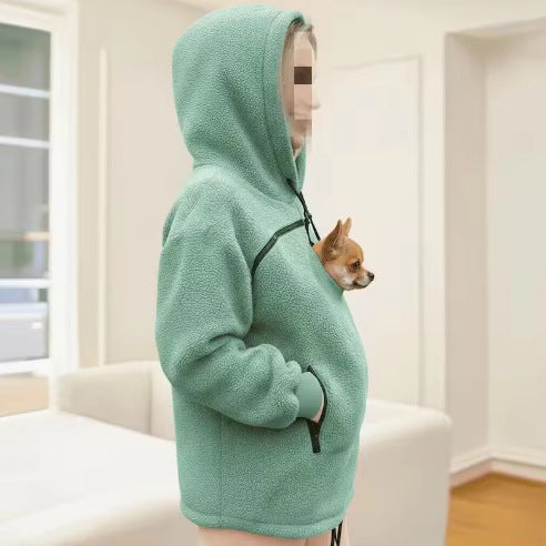A mint green fleece pet hoodie with a front zipper and a small dog peeking out of the chest pocket, shown in a bright indoor room.