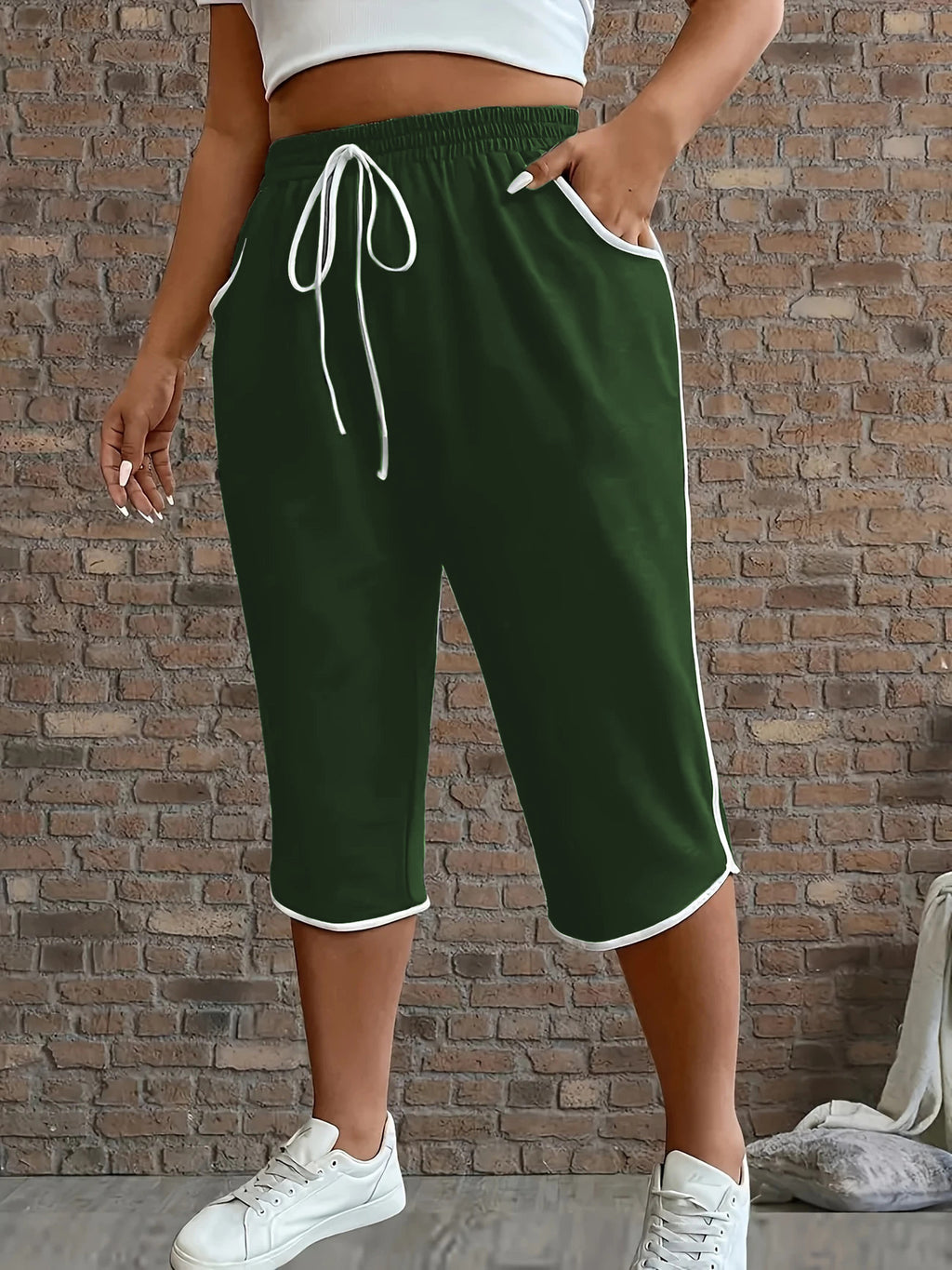 Person wearing green shorts with white drawstring and trim against a brick wall.