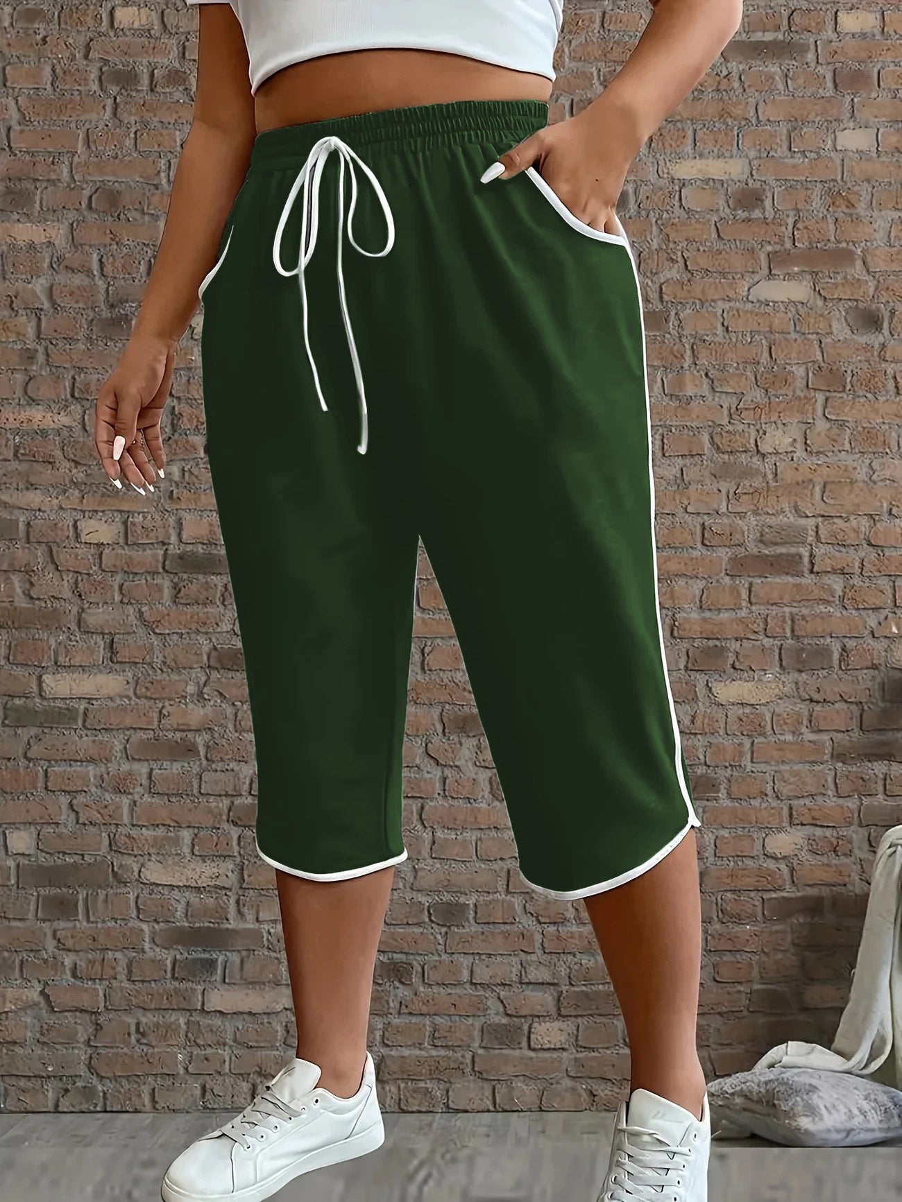 Person wearing green shorts with white drawstring and trim against a brick wall.