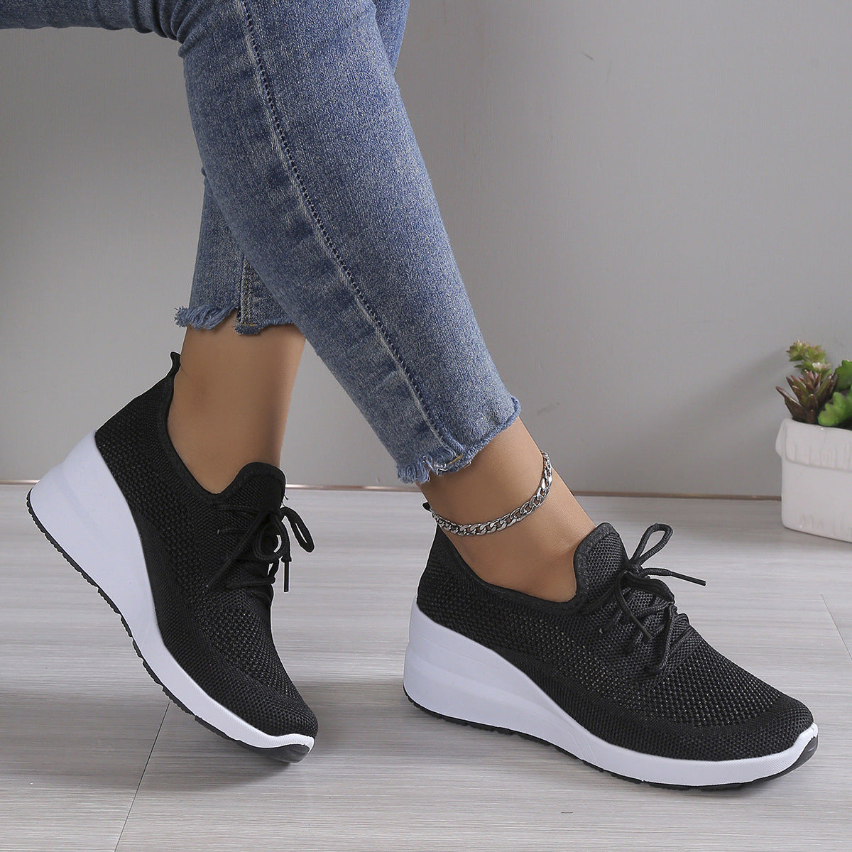 Black sneakers with white soles worn by a person on a neutral background