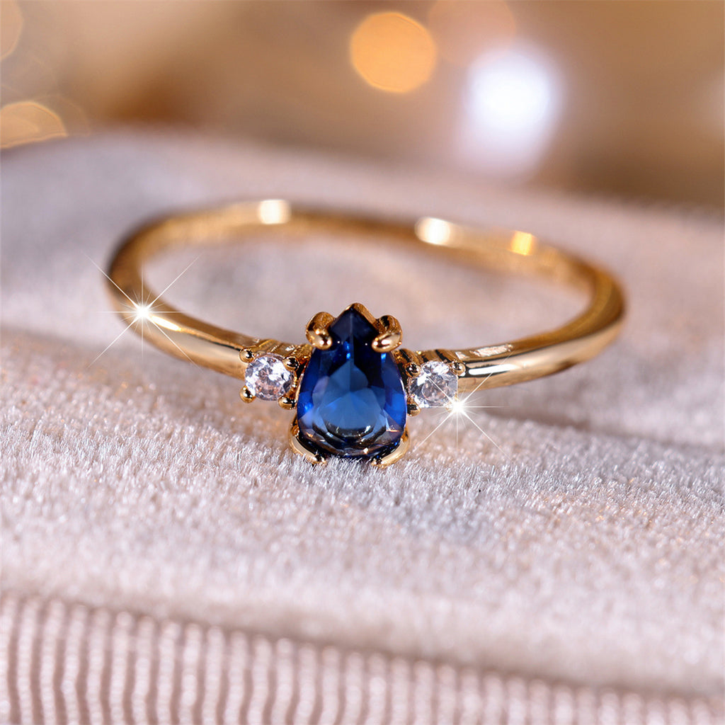 Gold ring with a blue gemstone and smaller diamonds on a textured surface.