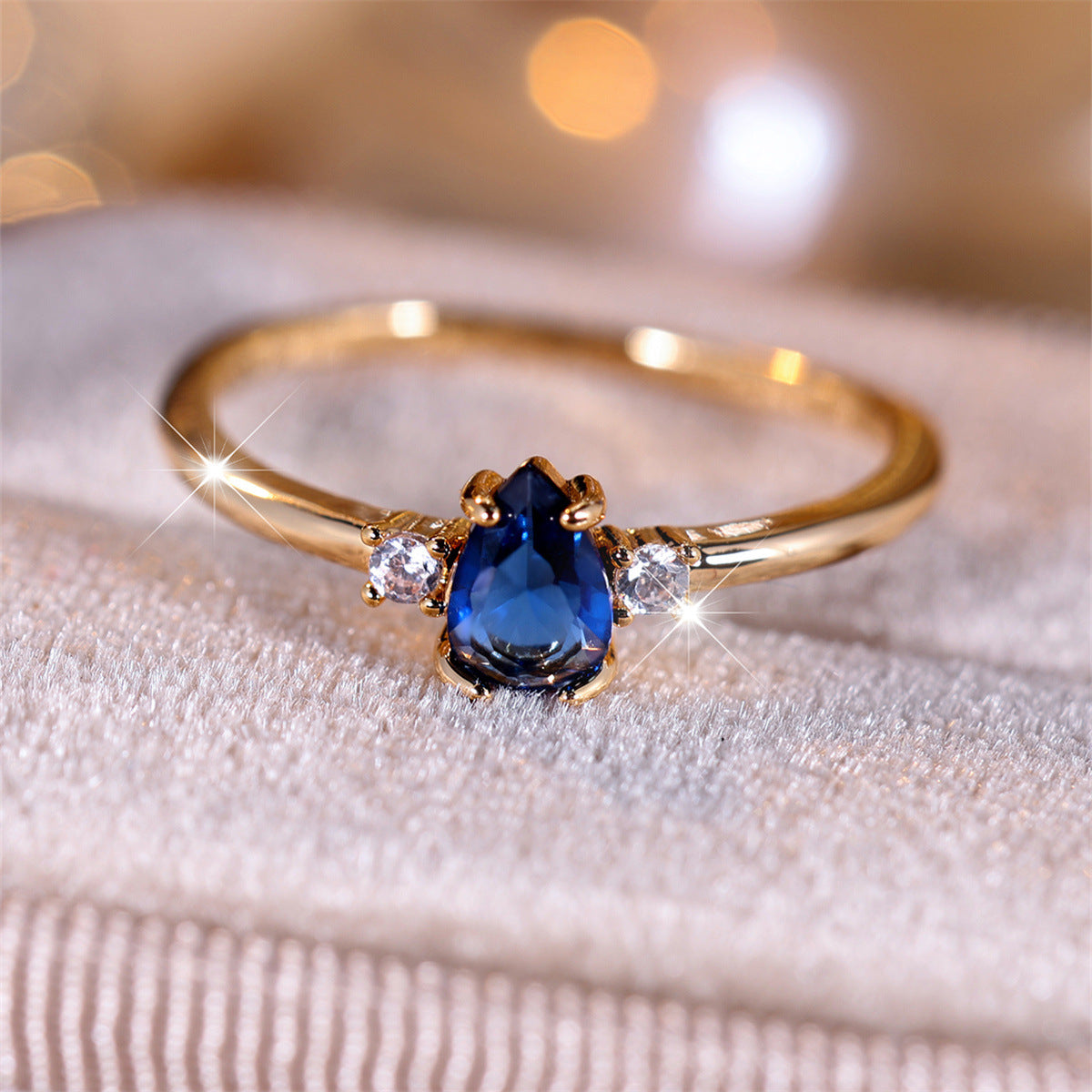 Gold ring with a blue gemstone and smaller diamonds on a textured surface.