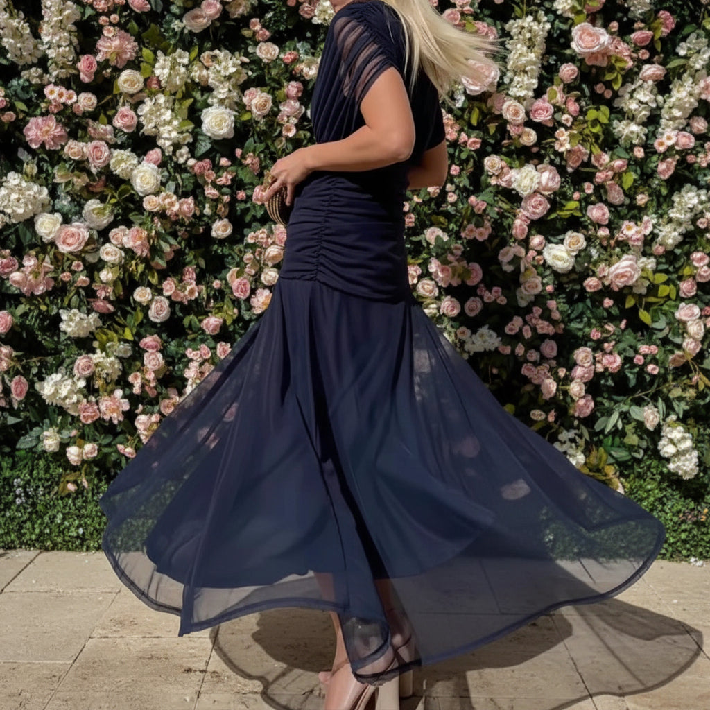 Woman wearing a flowing navy blue dress background of flowers and pavement.