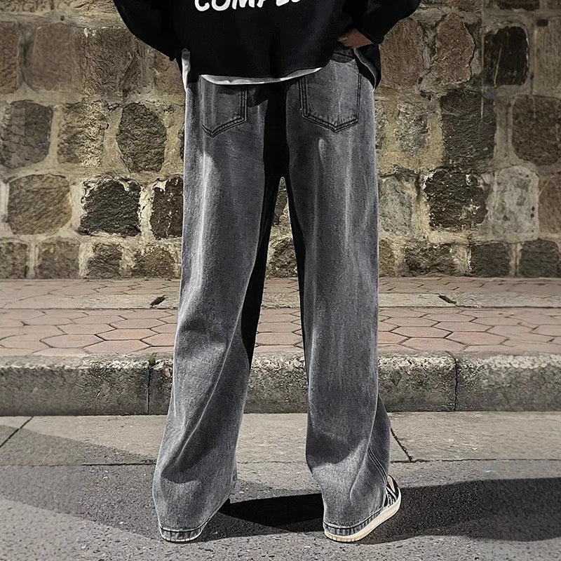 Person wearing black hoodie and gray wide-leg jeans standing against a stone wall.