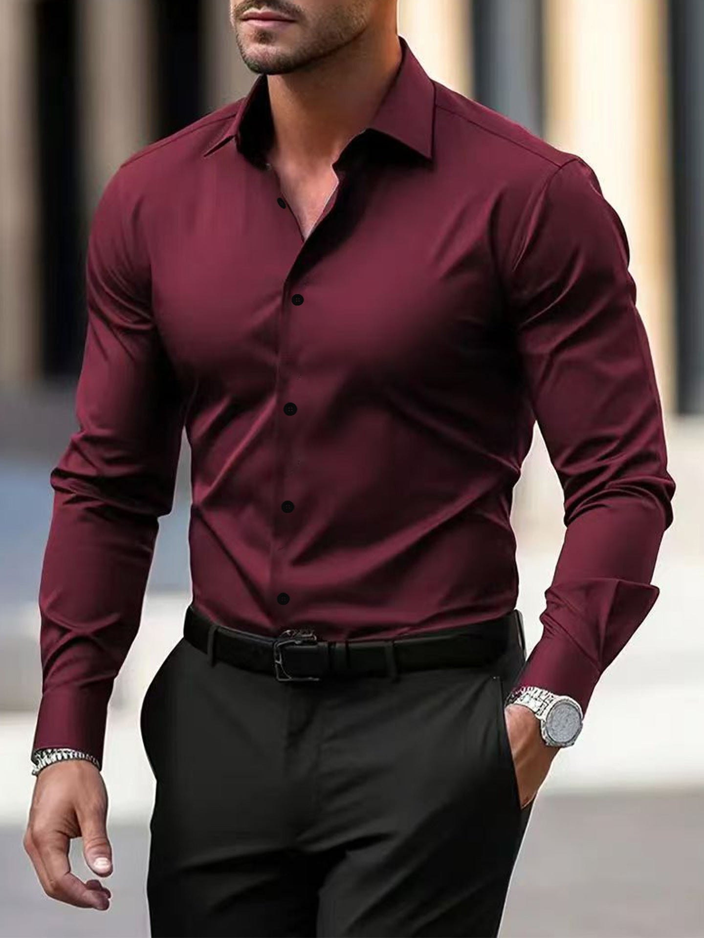 Man wearing a burgundy dress shirt and black pants with a blurred background