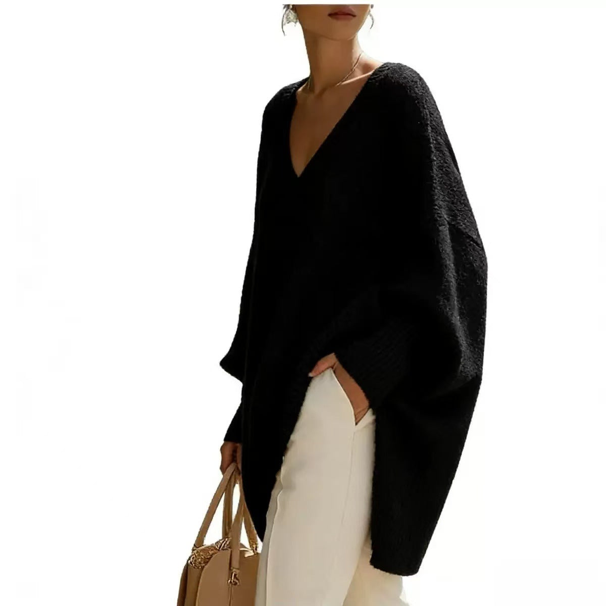 Person wearing a black poncho over a white outfit, holding a beige handbag on a white background