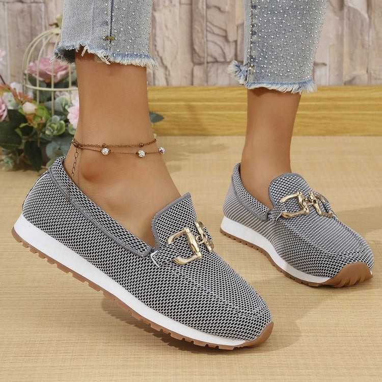 Gray loafers with gold accents worn by a person on a wooden floor.