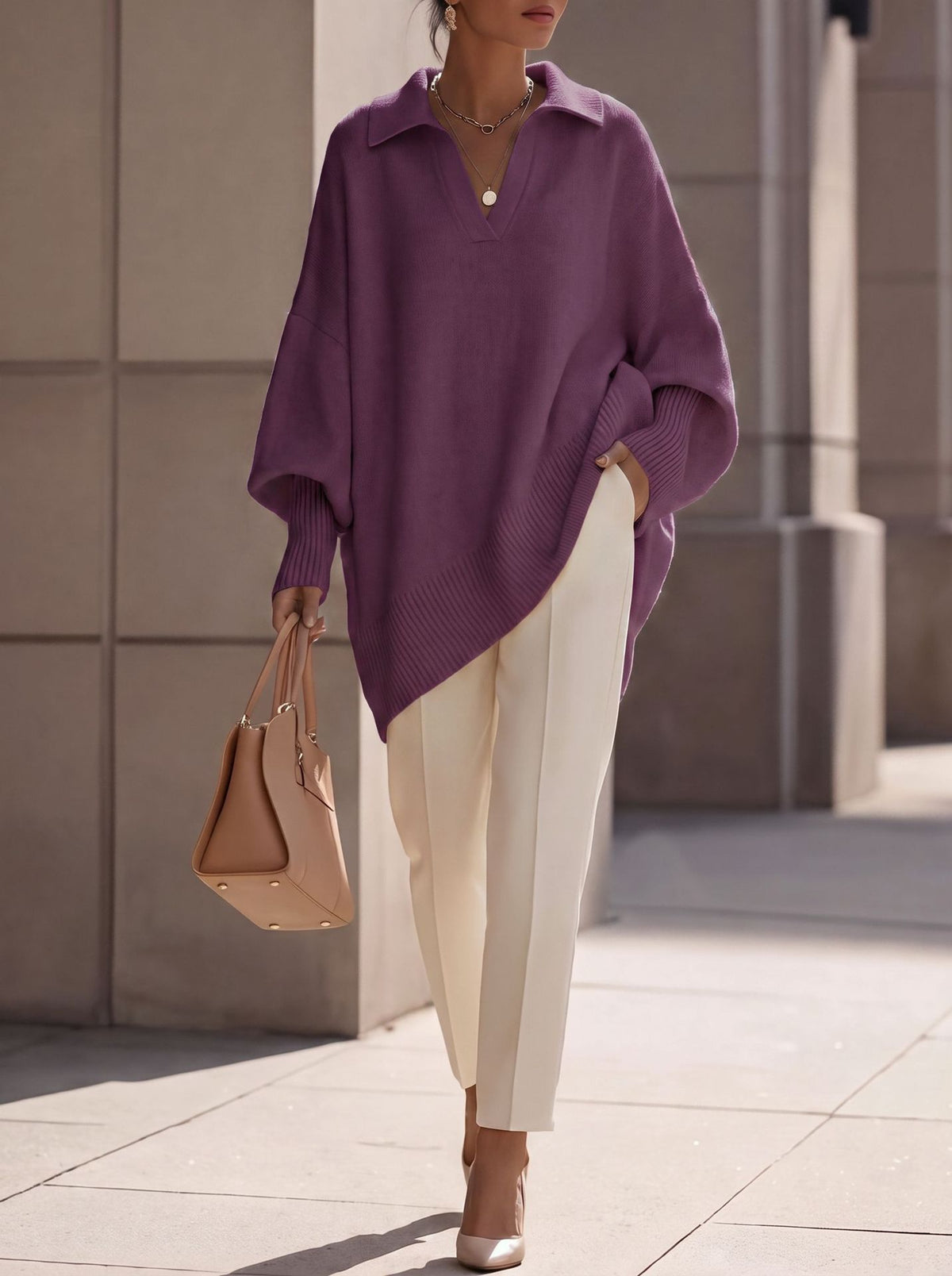 A woman wearing an oversized purple knit polo sweater, cream-colored trousers, and beige heels, carrying a tan leather handbag while walking outdoors.