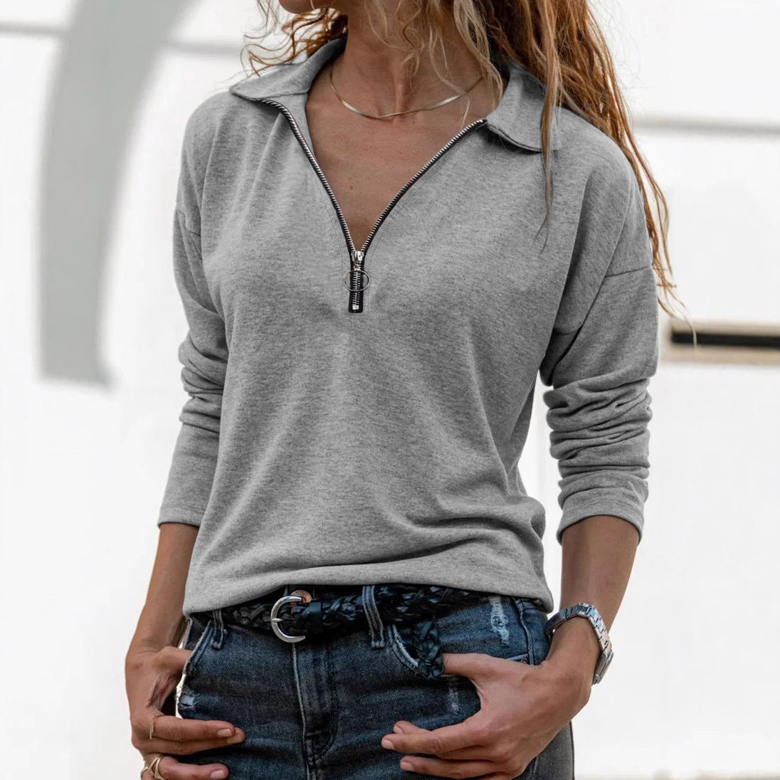 Person wearing a gray long-sleeve top with a zipper detail, standing indoors.