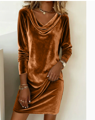 A woman wearing a long-sleeve cowl neck velvet mini dress in a warm rust brown color, styled with gold jewelry against a neutral indoor background.
