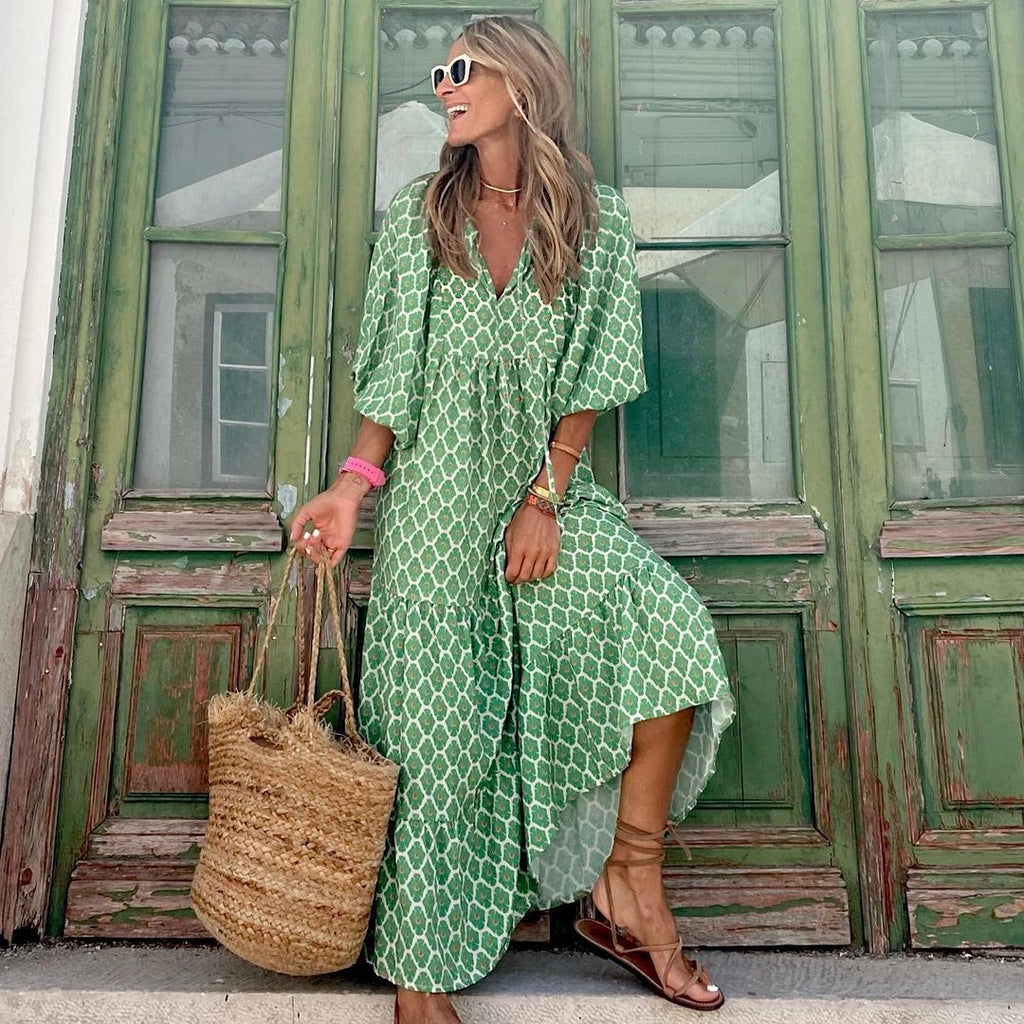 Woman in a green patterned dress holding a straw bag in front of a green door.