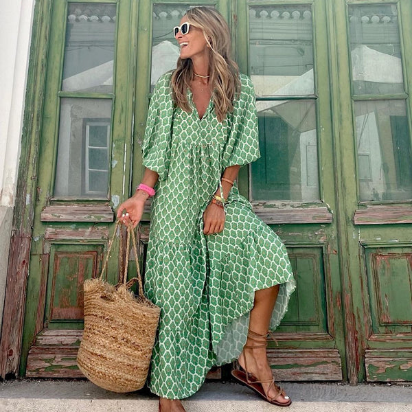 Woman in a green patterned dress holding a straw bag in front of a green door.