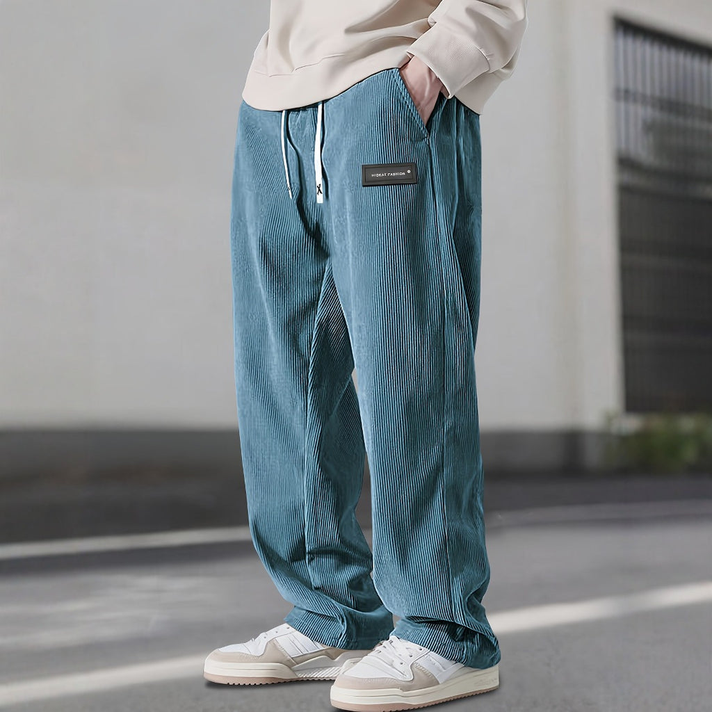Person wearing teal corduroy pants with a brand patch, standing on a street.