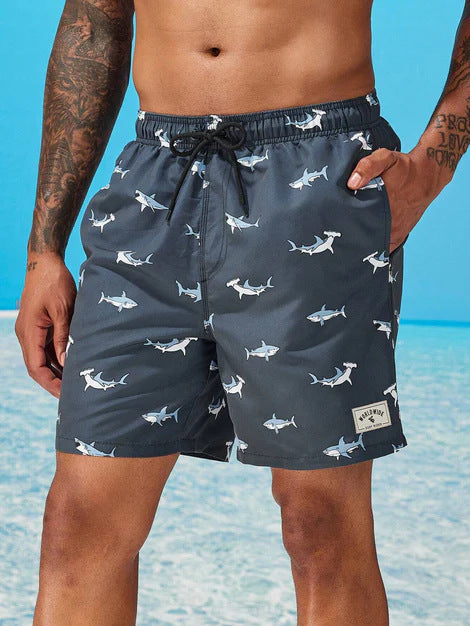 Person wearing navy swim shorts with shark pattern on a beach.