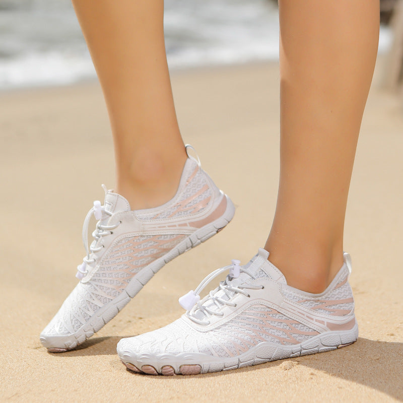 White sneakers on a person's feet standing on sand with water in the background