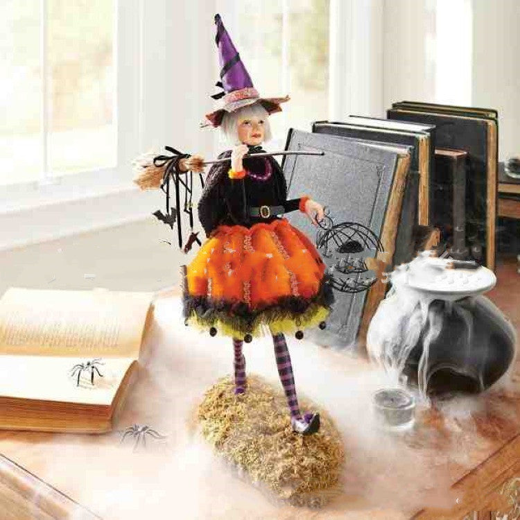 Halloween-themed doll in a witch costume with broom and hat, standing on a table with books and a vase.