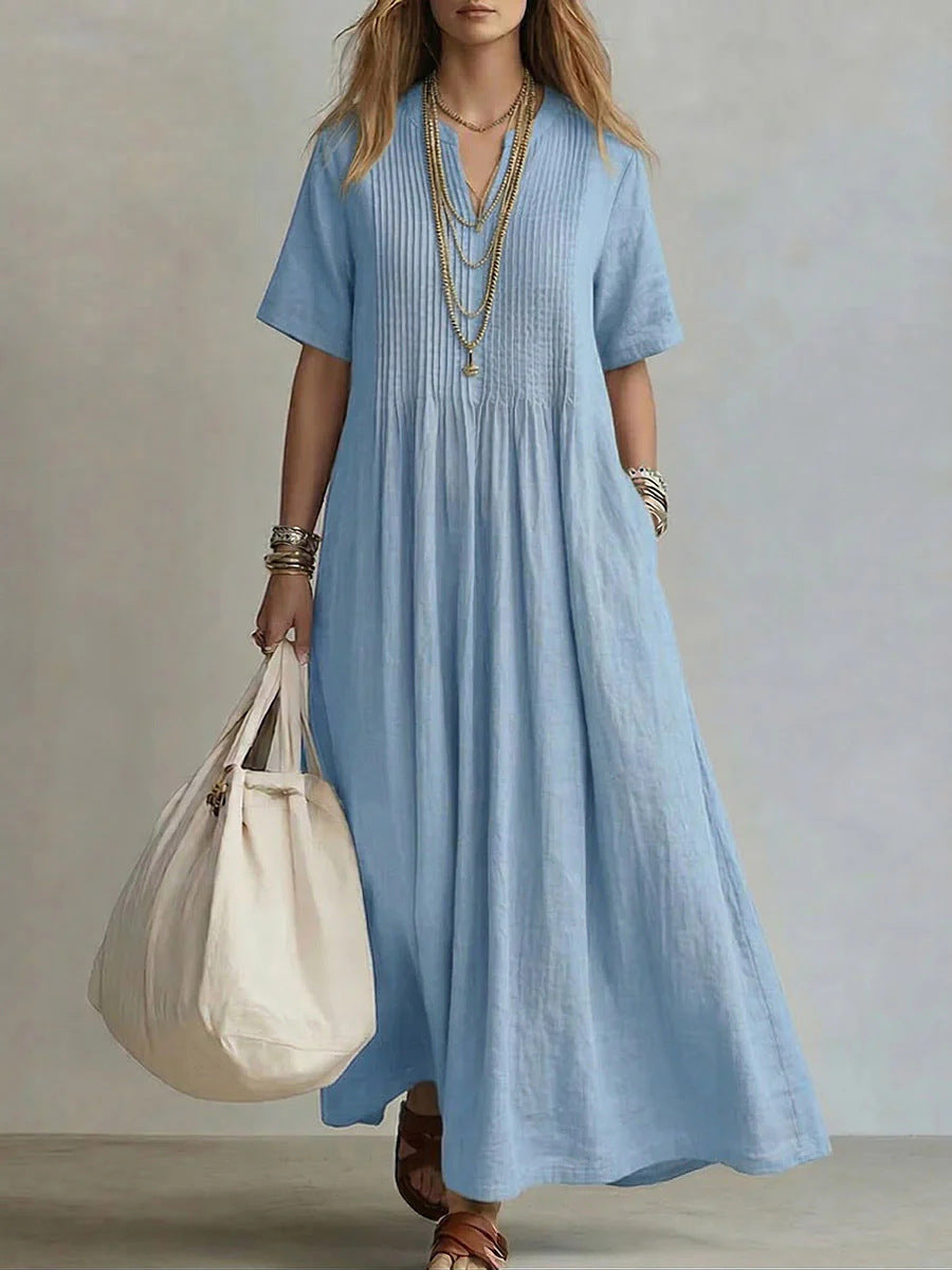 Woman wearing a long blue dress holding a beige bag against a neutral background