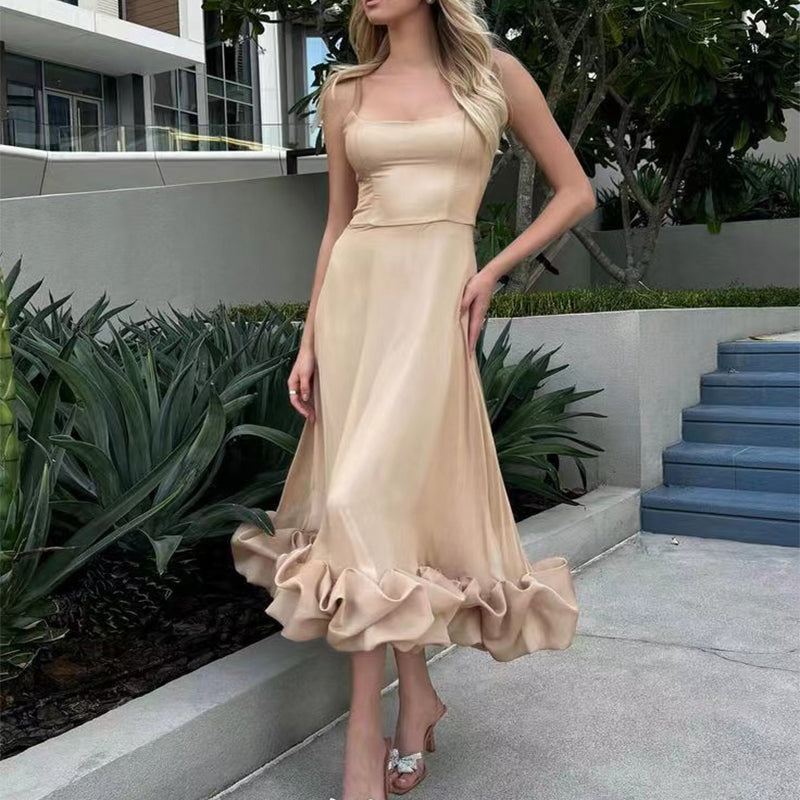 Woman wearing a beige dress standing outdoors with greenery and steps in the background