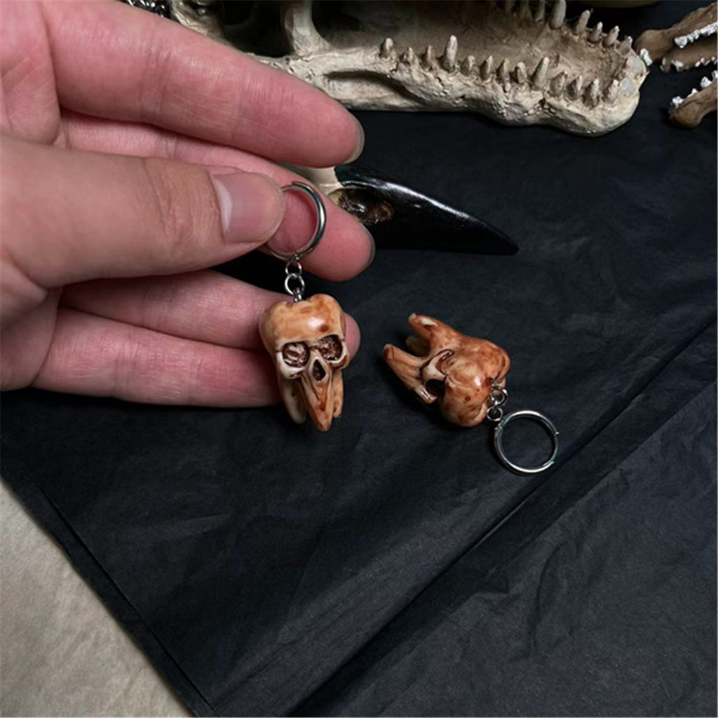 Hand holding a small animal skull keychain with another keychain on a dark surface.