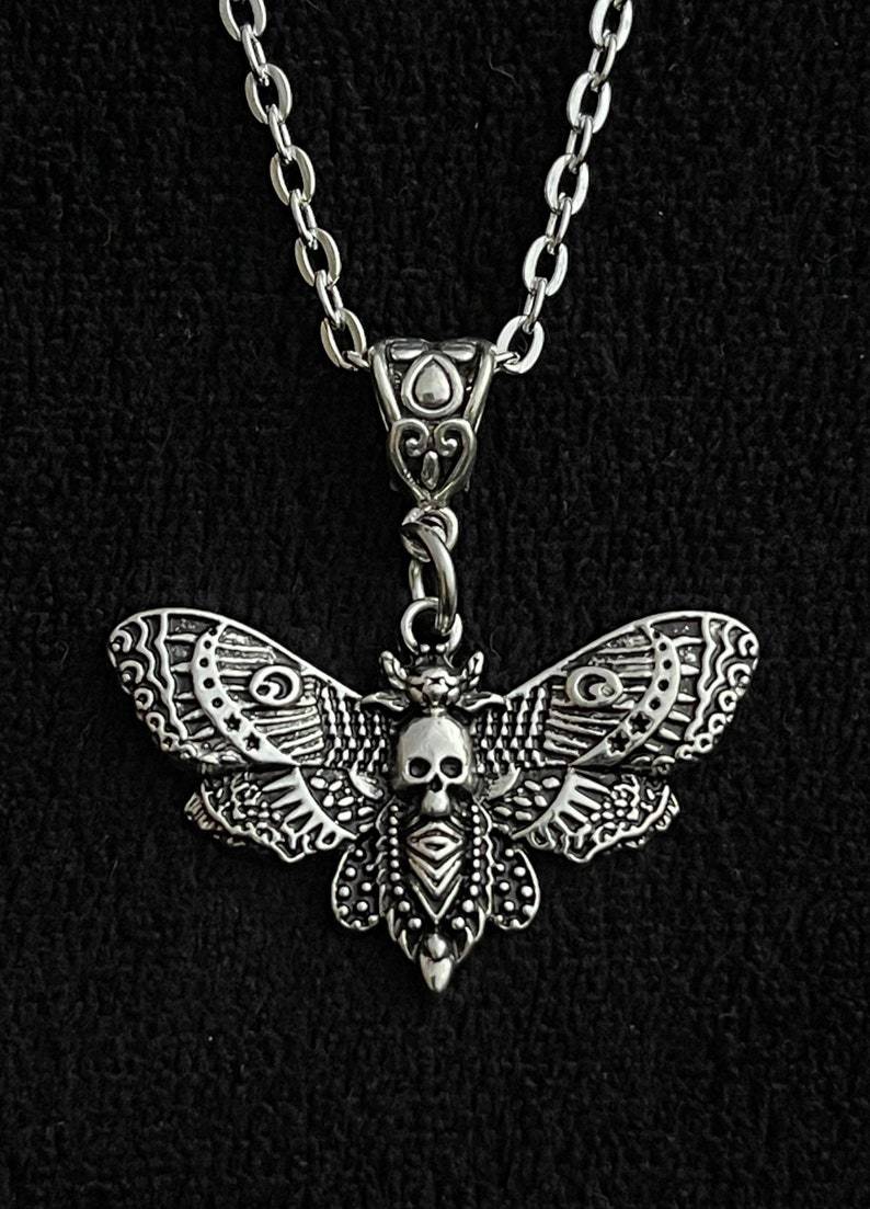 Silver moth-shaped pendant with skull design on a black background