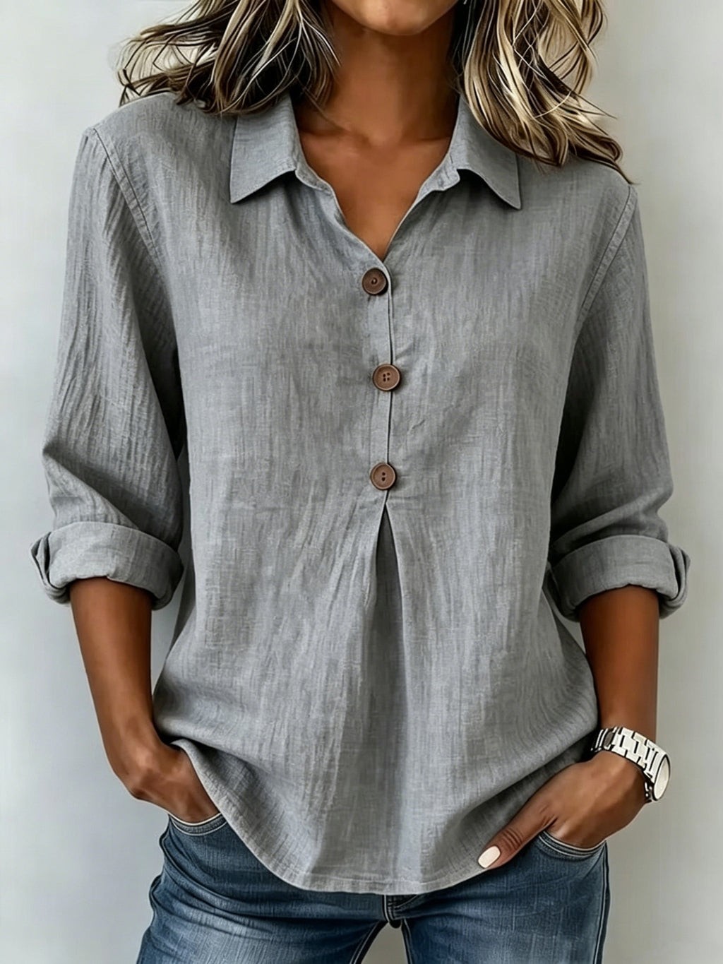 Person wearing a gray button-up shirt with rolled-up sleeves against a white background