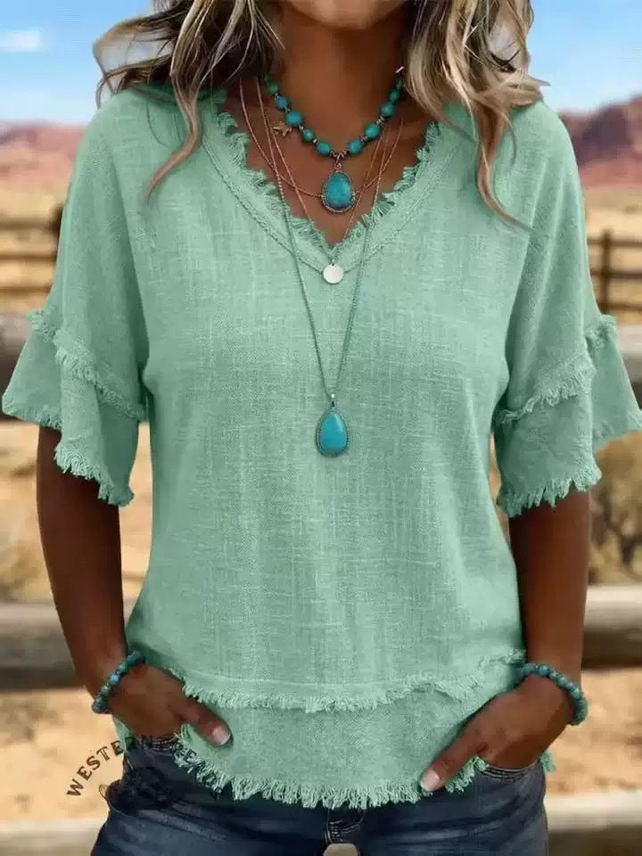 Person wearing a green blouse with fringe details and turquoise jewelry outdoors.