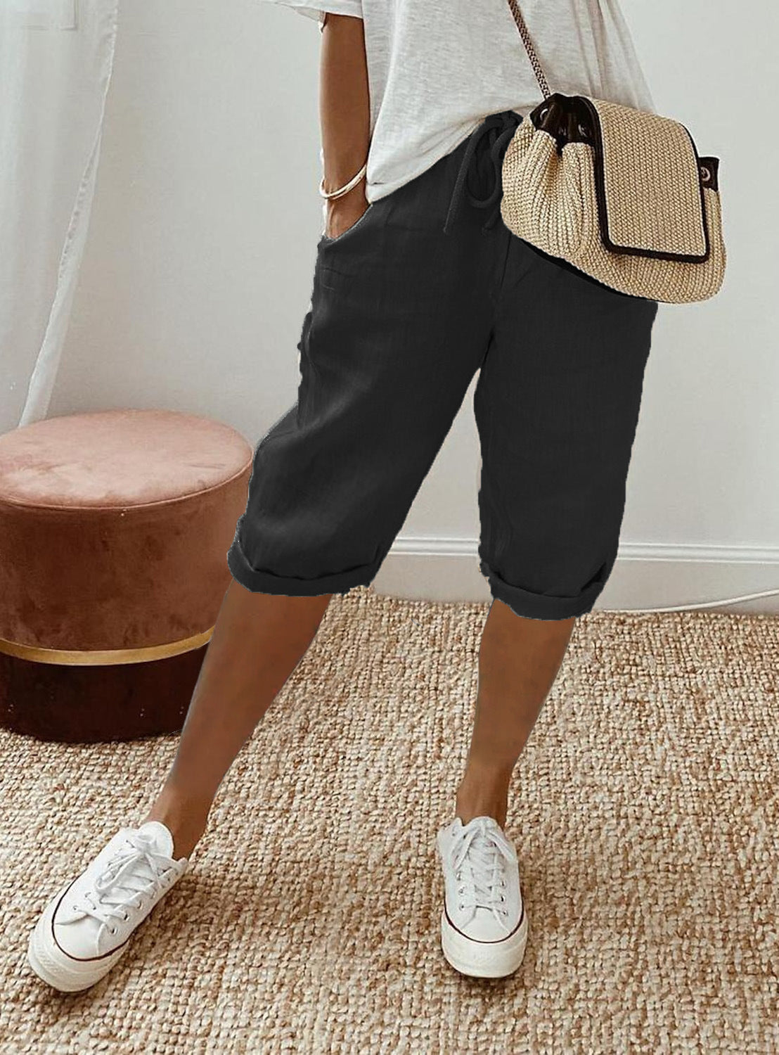 Person wearing black shorts, white sneakers, and a straw bag indoors.
