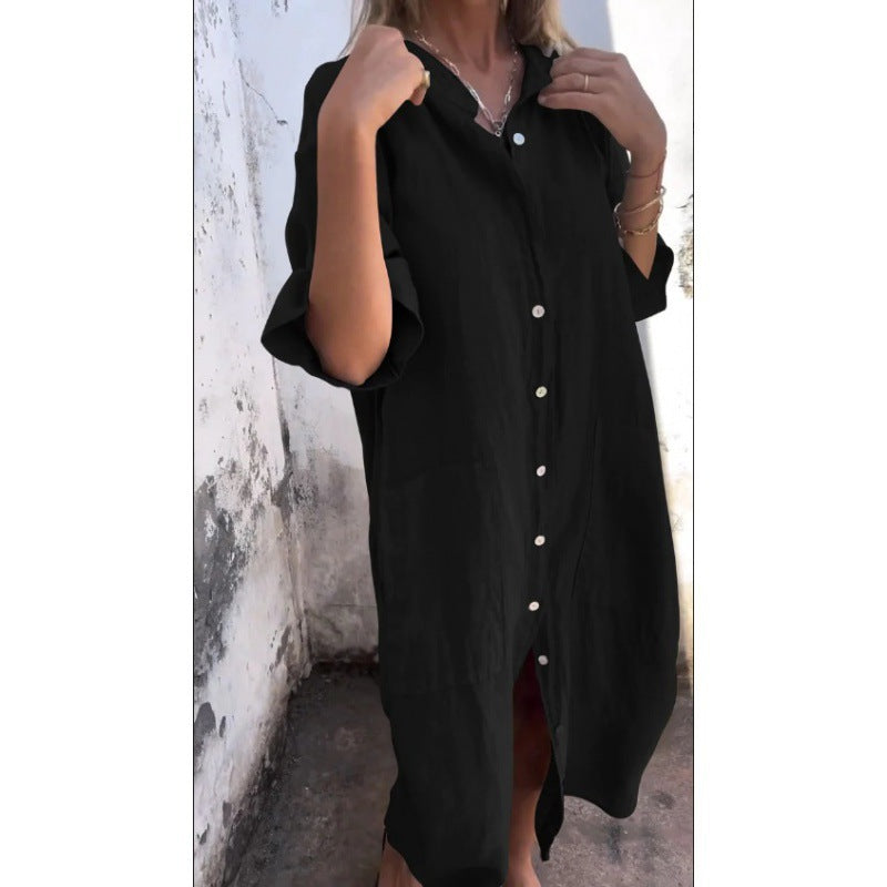 Person wearing a black button-up dress against a white wall.