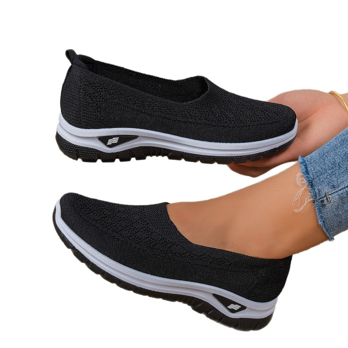 Black slip-on shoes with white soles worn by a person on a white background