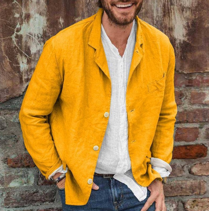 Man wearing a yellow jacket over a white shirt against a brick wall.
