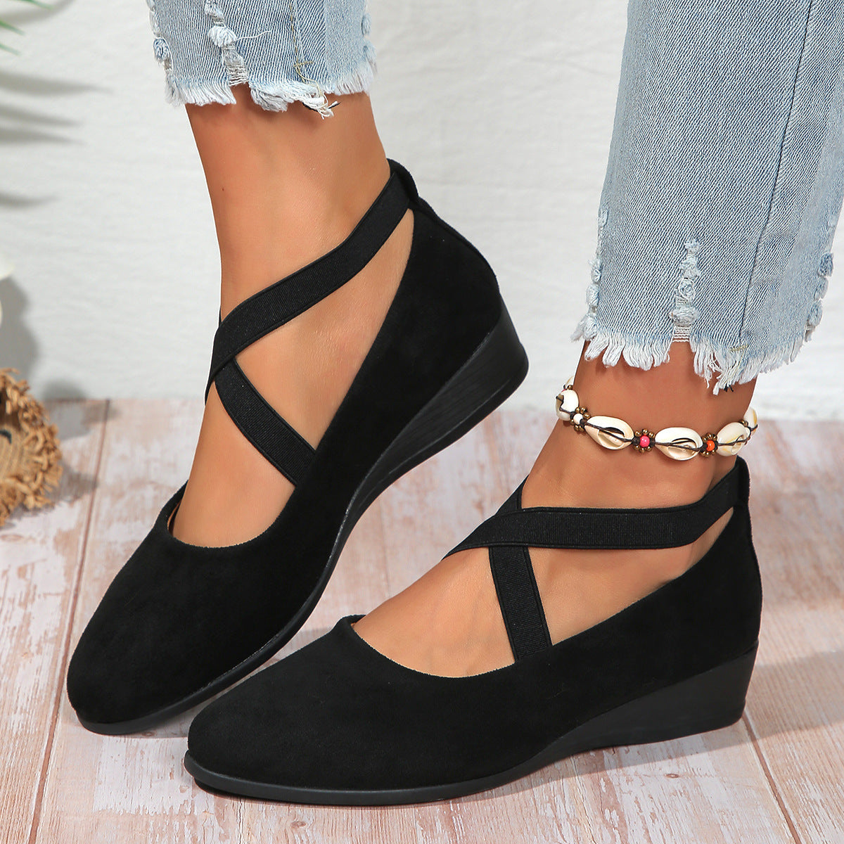 Black wedge sandals worn with light blue jeans on a wooden floor.