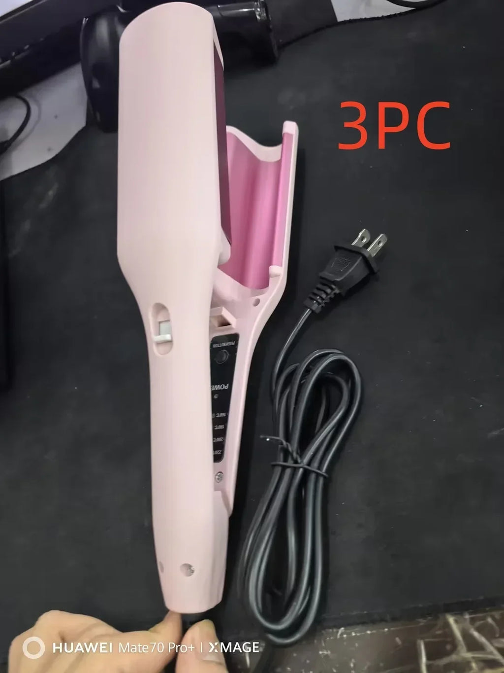 Pink electric hair curler with power cord on black surface, hair styling tool