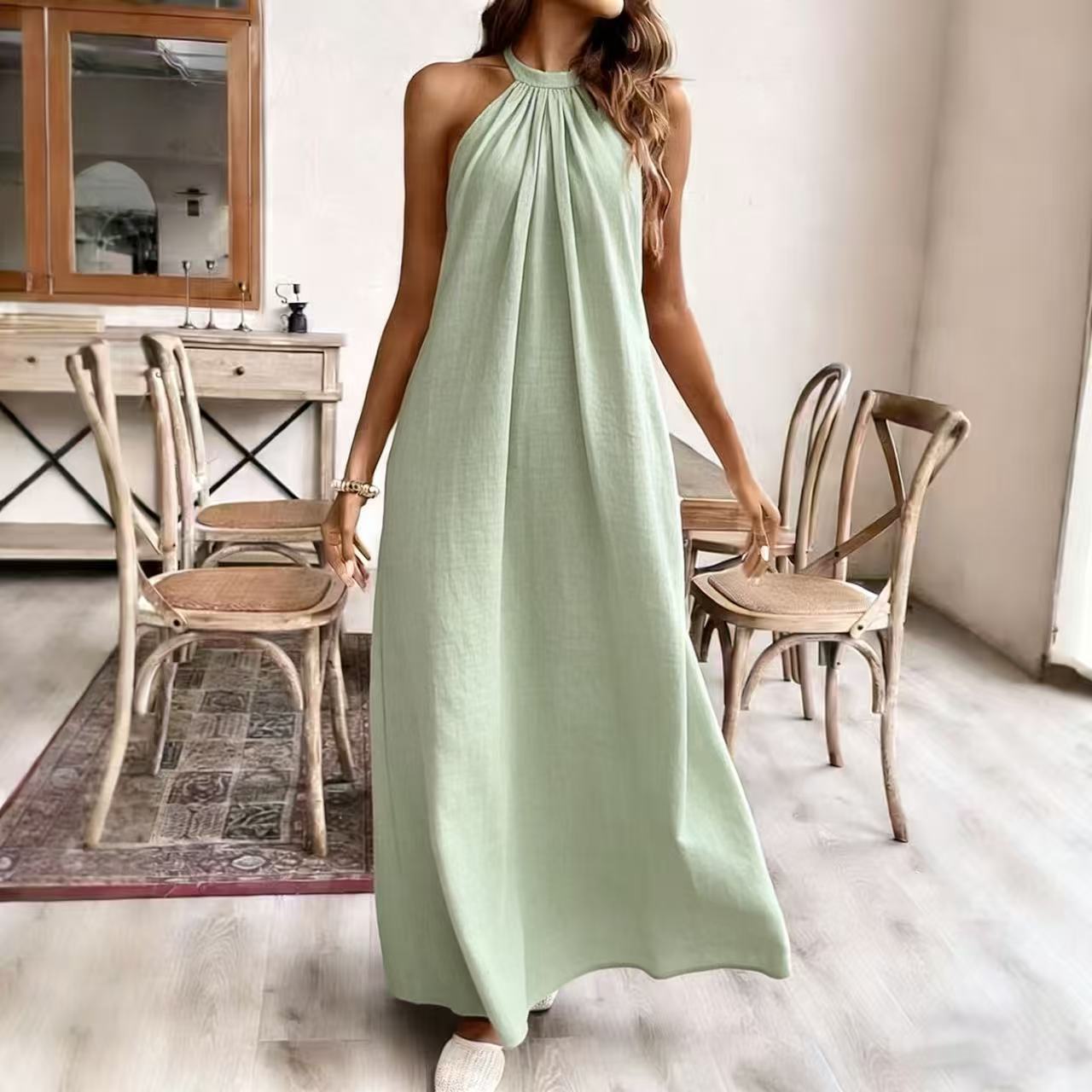 Woman wearing a long light green dress in a room with wooden chairs and a table.