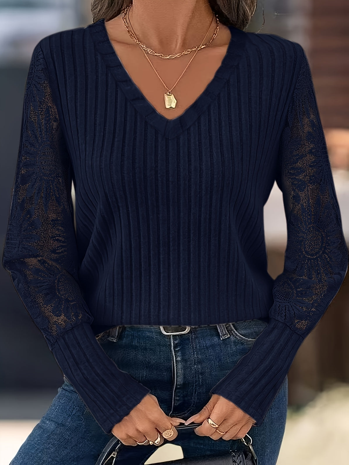 A woman wearing a navy blue ribbed knit sweater with lace sleeves, paired with blue jeans and layered gold necklaces.