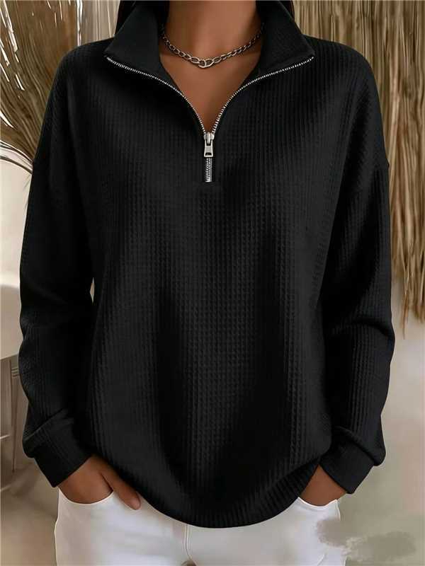 A person wearing a black quarter-zip long-sleeve pullover with a textured waffle knit pattern and silver zipper trim, paired with white pants.