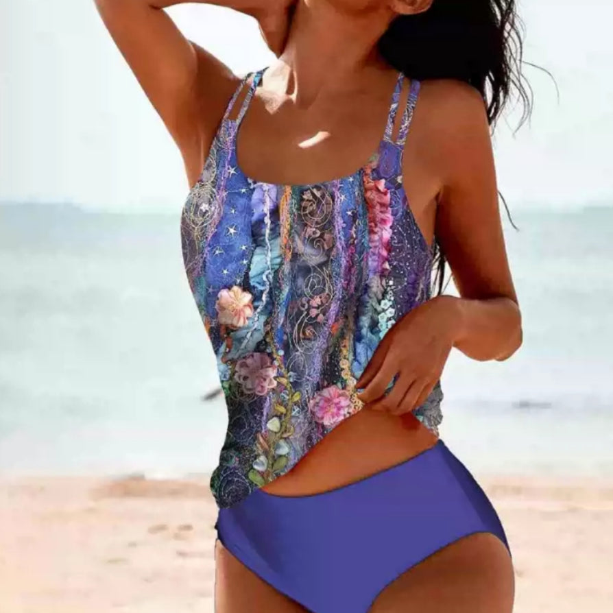 Woman wearing a colorful floral tankini top and blue high-waisted bikini bottom on a beach.
