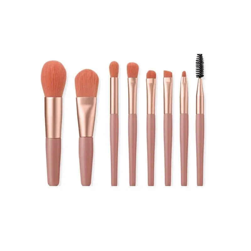 Set of eight rose gold makeup brushes with soft bristles and pink handles on white background.