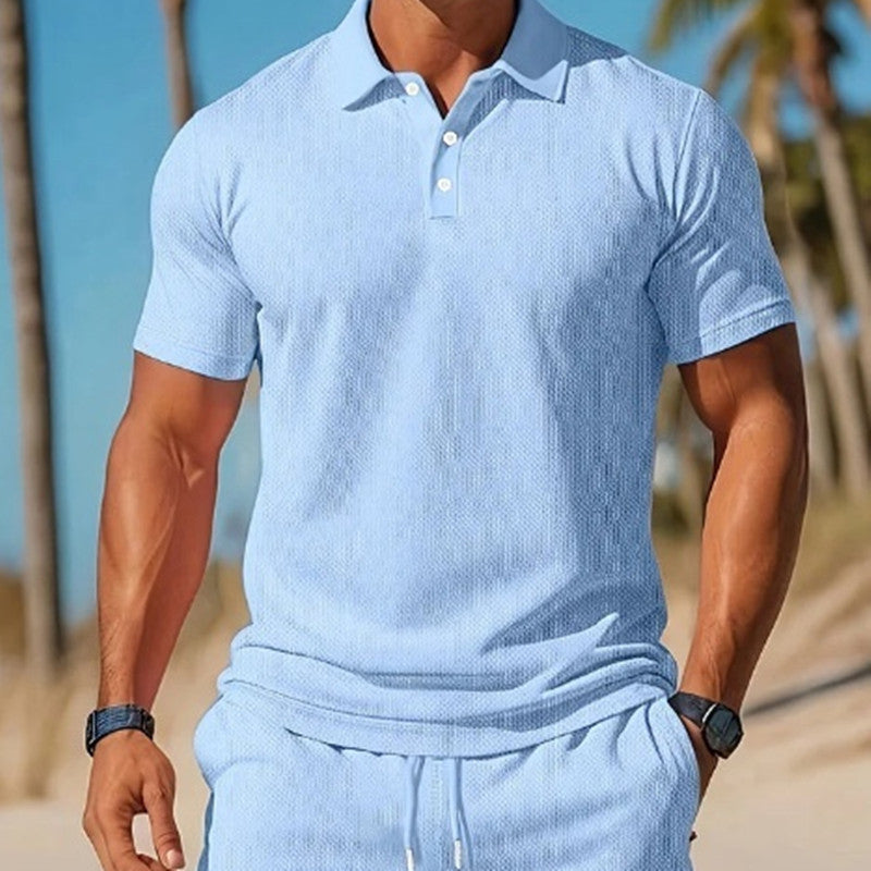 Man wearing a light blue textured polo shirt and pants on a beach.
