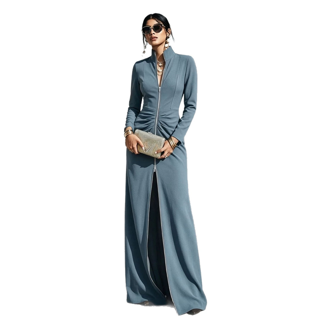 A woman modeling a long-sleeve, floor-length blue dress with a front zipper, high collar, and a front slit, holding a metallic clutch against a plain white background.