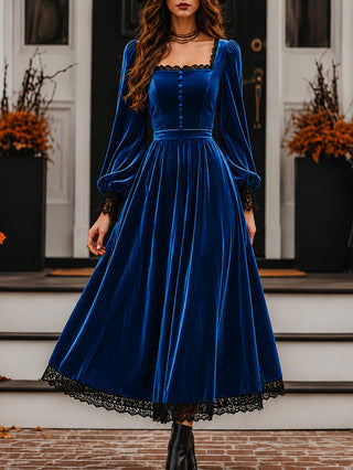 Woman wearing a blue velvet dress with long sleeves and black lace details in front of a house.