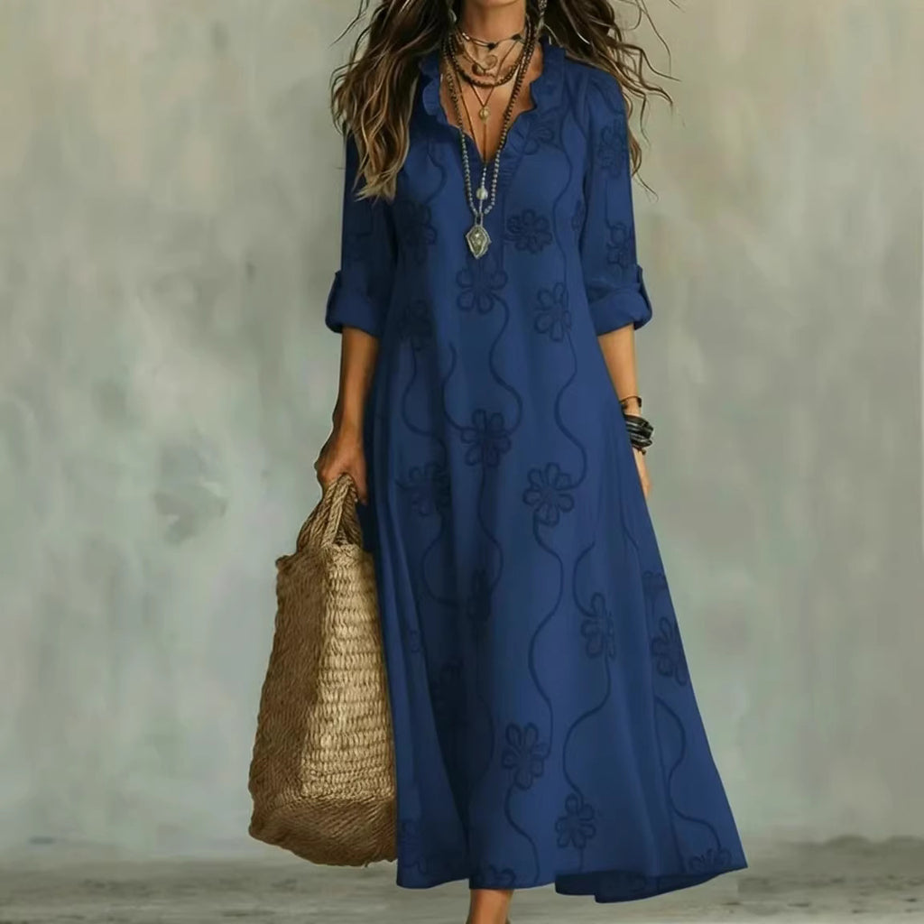 Woman wearing a blue dress with floral patterns, holding a woven bag against a neutral background