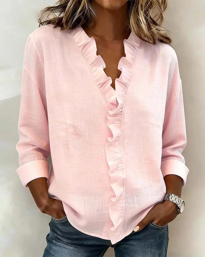 Person wearing a light pink blouse with ruffled details against a neutral background