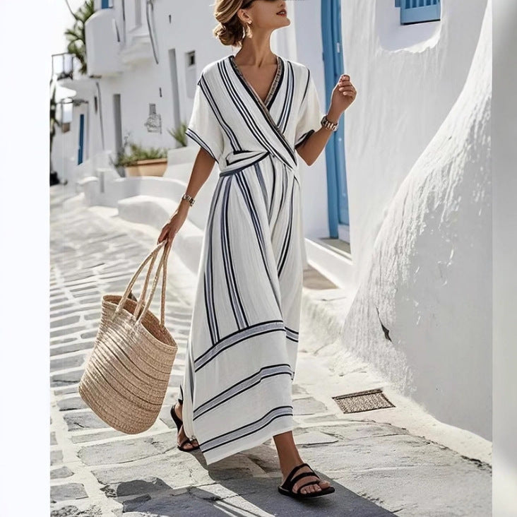 Woman in a white and black striped dress walking on a sunlit street with white buildings.