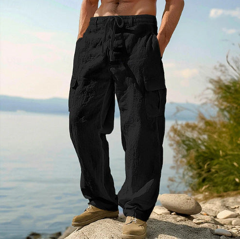 Person wearing black cargo pants standing by a body of water with mountains in the background.
