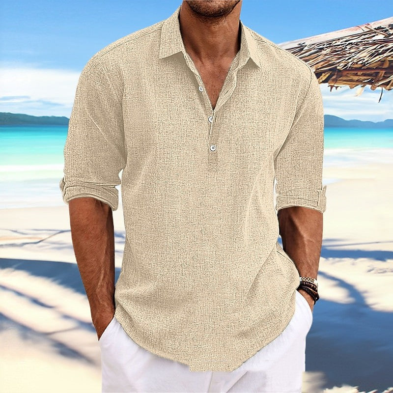 Man wearing a beige short-sleeve shirt and white pants on a beach.